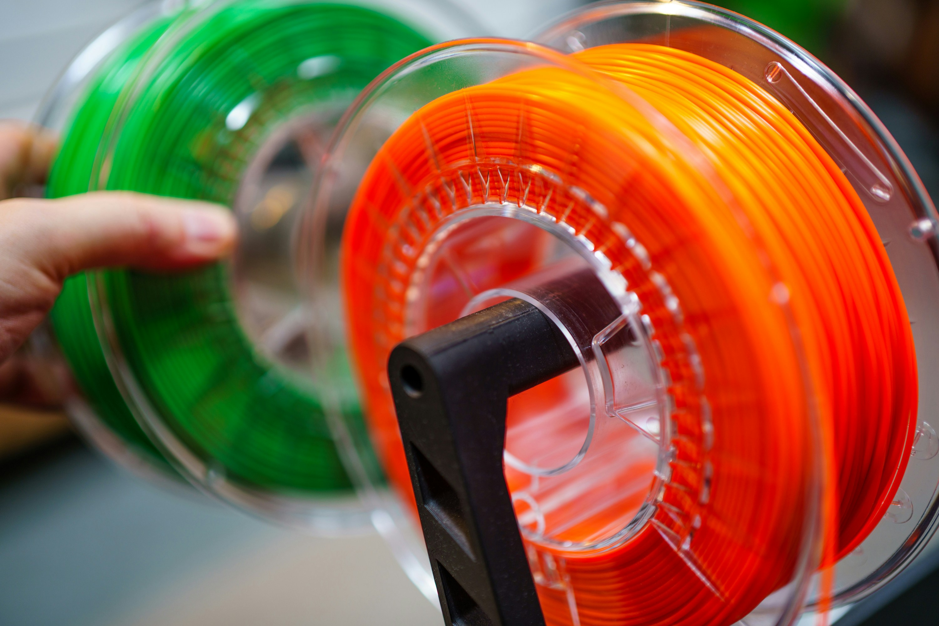 Close-up of orange and green filament spools on transparent reels.